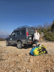 A Land Rover Discovery 4x4 vehicle parked on a rocky trail in Galicica National Park with paragliding gear and a smiling passenger.