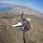 Wide-angle aerial GoPro shot of a tandem paraglider soaring high above the city of Ohrid and the blue waters of Lake Ohrid.