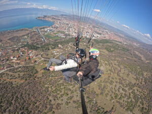 Wide-angle aerial GoPro shot of a tandem paraglider soaring high above the city of Ohrid and the blue waters of Lake Ohrid.