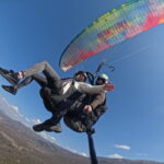 Perspective from below of a colorful rainbow-patterned paraglider wing during a tandem flight over the Macedonian mountains.