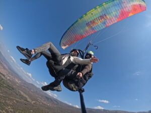 Perspective from below of a colorful rainbow-patterned paraglider wing during a tandem flight over the Macedonian mountains.